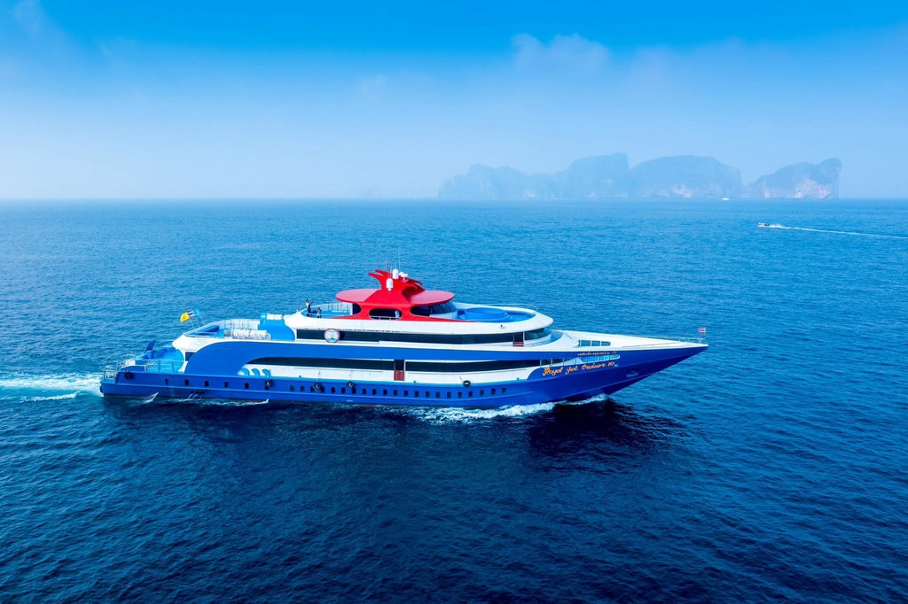 Blue and white cruise ship with a red top sailing on calm blue waters with distant mountains.