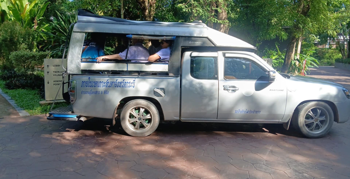 Silver camper van with people inside on a road surrounded by greenery