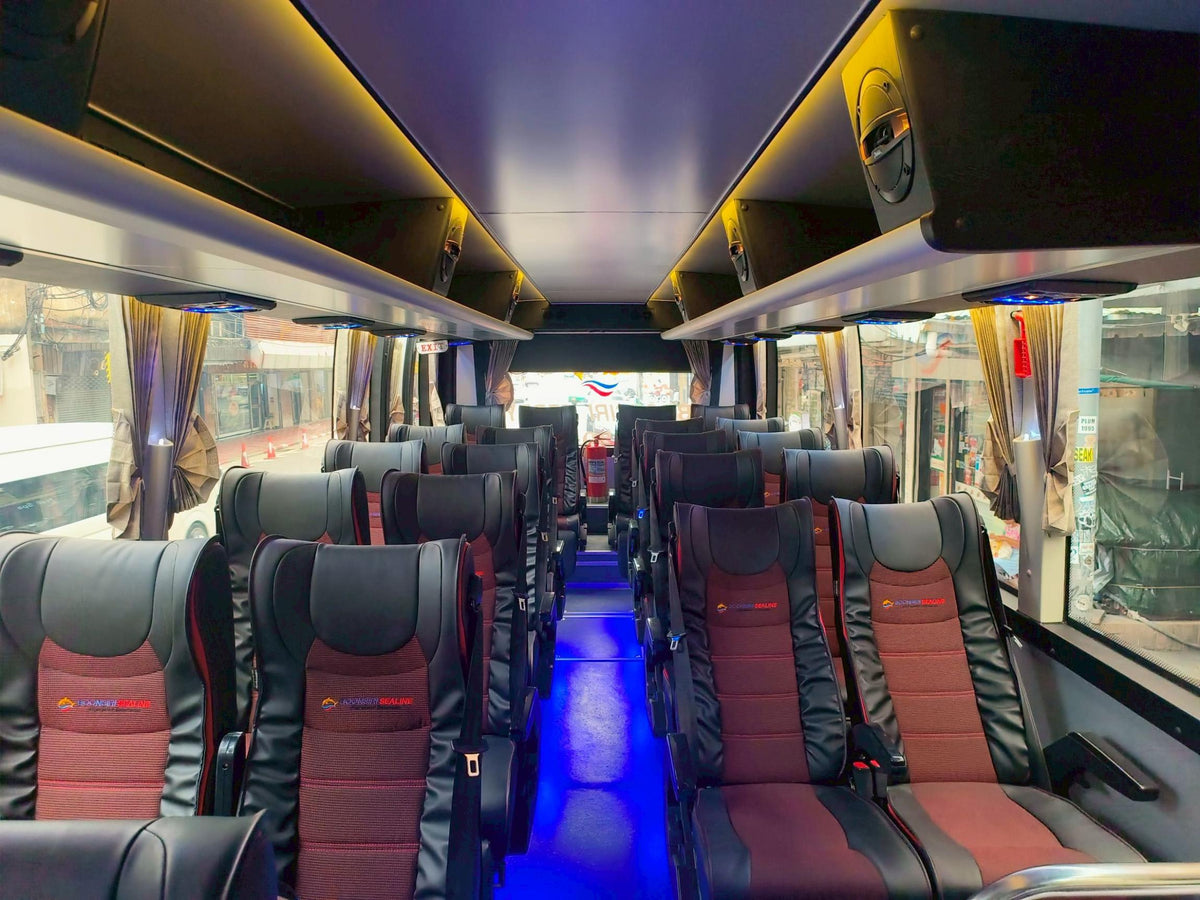 Coach interior with red and black passenger seats, overhead luggage racks and blue aisle lighting