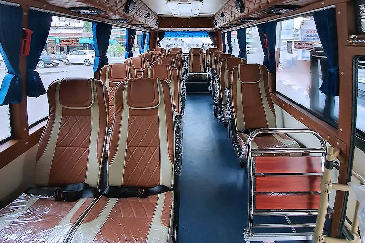 The interior of a passenger bus with rows of brown and beige quilted seats, dark blue curtains, a blue floor, and a metal luggage cart near the right side.