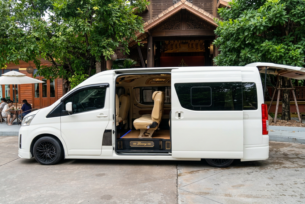 White passenger van with an open sliding door showing beige seats outside a wooden building