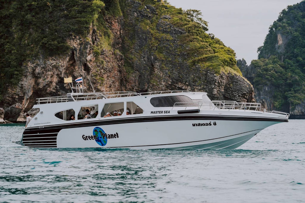 Boat named 'Green Planet' on water with rocky cliffs in the background