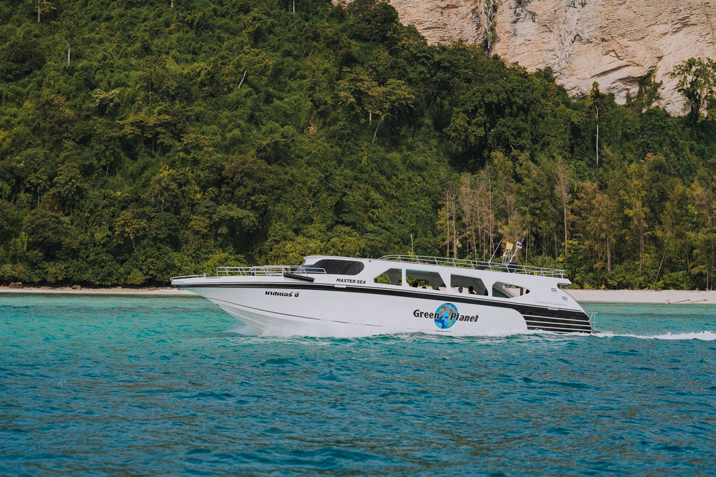 White boat with green logo on a body of water surrounded by trees and cliffs
