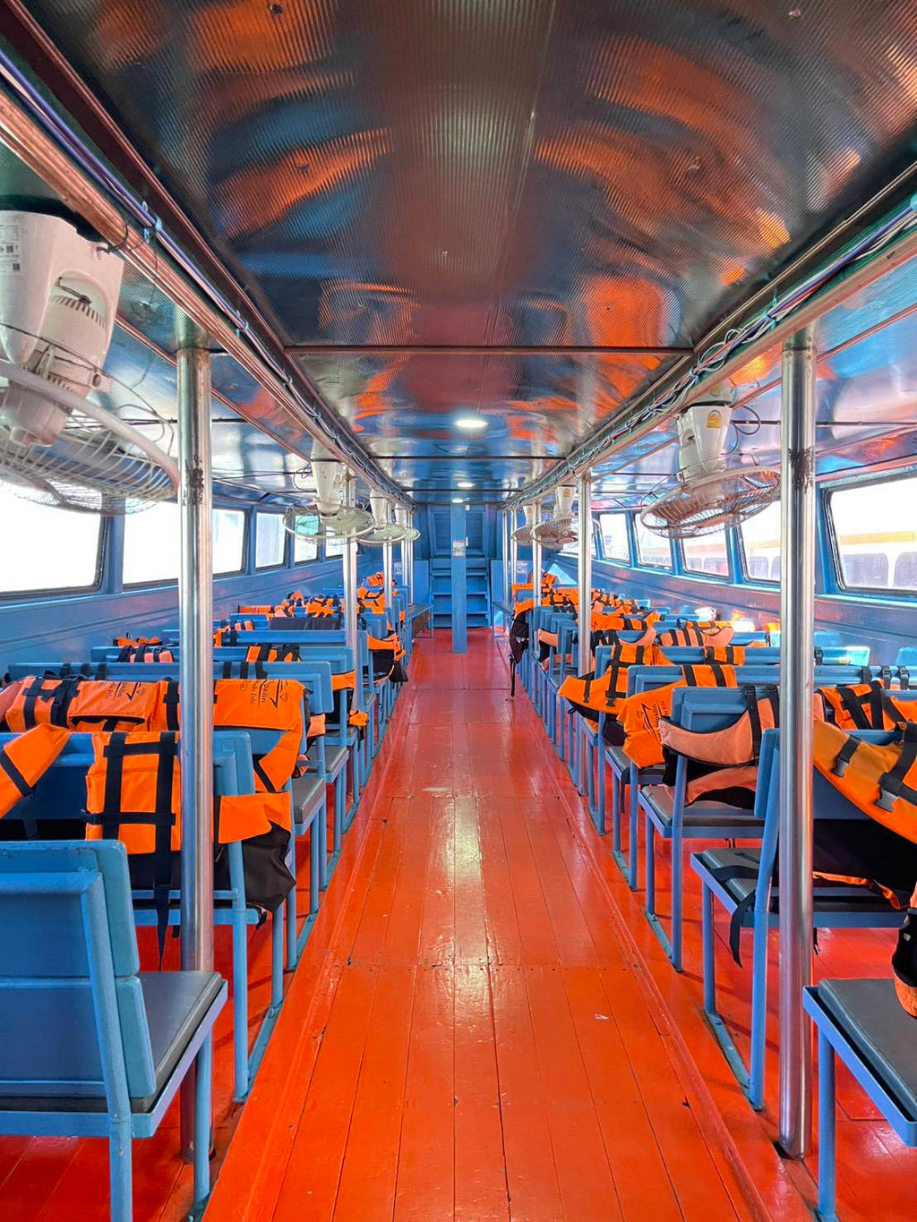 Ferry cabin with blue seats, orange life jackets and a central aisle