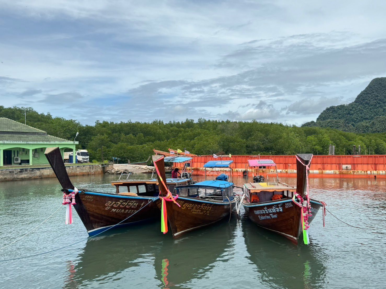 Three traditional wooden boats tied together in a harbor with a scenic background.