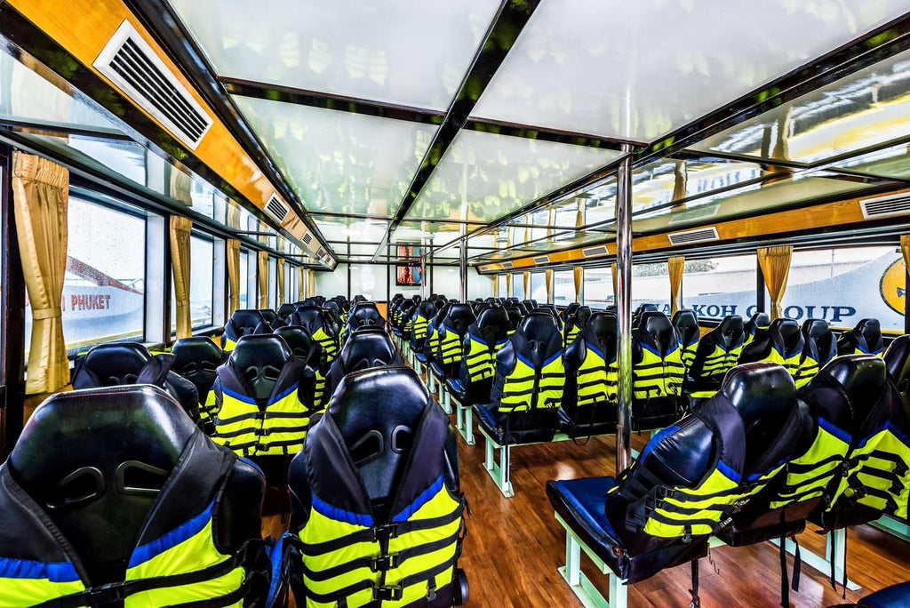 Rows of black and neon yellow life jackets worn by passengers seated inside a large boat cabin with wood flooring and large windows.
